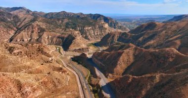 Utah 'taki Price Kanyonu' nun yüksek uçurumları arasındaki mavi gökyüzünün altındaki otobanın hava aracı görüntüsü..