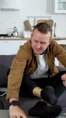 Evdeki kanepede oturan adam. Genç adam evde dinleniyor, çoraplarını fırçalıyor.