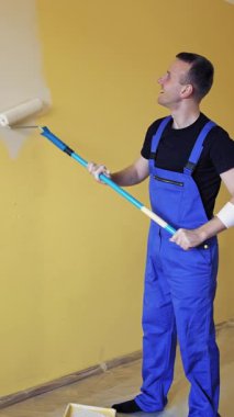 Duvarı boya rulosuyla boyayan adam. Duvarları boyayan yakışıklı genç adam, yeniden dekore odası.