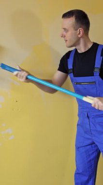 Adam duvarları silindirle boyuyor. Ressam iş yerinde duvarları silindirle boyuyor.