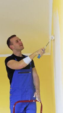 İş yerindeki adam duvarları boyuyor. Üniformalı işçiler duvarları boya rulosuyla boyuyor.