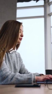 Esmer ofis çalışanı bilgisayarında daktilo yazıyor. Kadın dikkatini işine veriyor ve gözlükleri masadan alıyor. Düşük açı. Dikey video