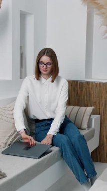 Kanepede oturan esmer kadın laptopunu açıyor. Bayan aleti kucağına alır ve çalışmaya başlar. Dikey video