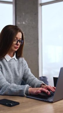 Uzun saçlı esmer, masa başında oturup bilgisayarında yazı yazıyor. Geniş ofiste çalışan bir iş kadını. Dikey video