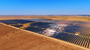 Açık arazide büyük bir güneş enerjisi santrali. Açık mavi gökyüzü altında binlerce fotovoltaik paneli olan devasa bir güneş enerjisi santralinin havadan görünüşü.