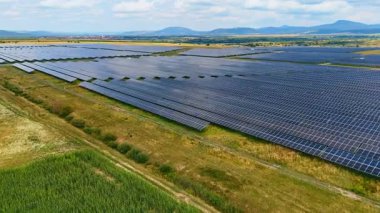 Mavi gökyüzü ve bulutların altında güneş enerjisi alanı. Güneşli bir günde dağınık bulutlarla yenilenebilir elektrik üreten bir güneş paneli görüntüsü..