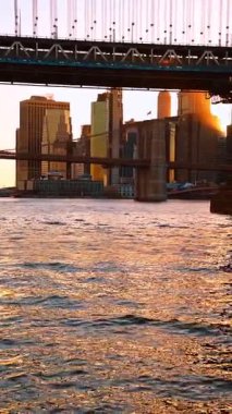 Gün batımında Doğu Nehri 'nin su manzarasından görüntüler. Manhattan Köprüsü ve Brooklyn Köprüsü alçak açılı görünüyor. Dikey video.