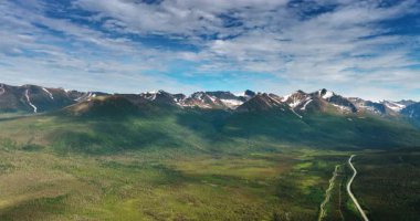 Bulutların gölgelediği inanılmaz dağların ikonik manzarası. Dağ eteğindeki bir vadi otobanın yanından geçti. Alaska, ABD. Hava görünümü.