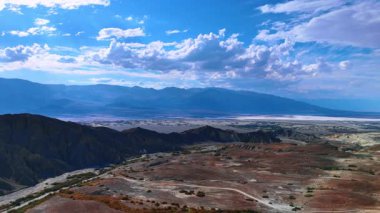 Sıcak güneşin göz kamaştırdığı uçsuz bucaksız çölün nefes kesici manzarası. Yukarıdaki mavi gökyüzünde beyaz pofuduk bulutlar. Death Valley Ulusal Parkı 'nın havadan görüntüsü, Kaliforniya, ABD.