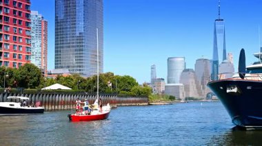 Jersey City, ABD, 1 Temmuz 2025: Büyük yatın yanında nehir kenarına giden bir grup insanla küçük kırmızı yelkenli. Jersey City 'de yelkencilik sporu. Arkaplanda Manhattan gökdelenleri.