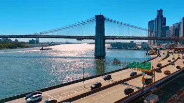 East River kıyısındaki yolların görüntüleri. Otobanlarda bir sürü araba var. Mavna Brooklyn Köprüsü 'nün altından geçiyor..