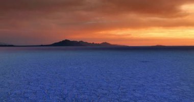 Gün batımında tuzlu manzaranın üzerindeki görüntüler maviye boyandı. Turuncu gökyüzüne karşı dağların siyah siluetine yaklaşıyoruz. Bonneville Salt Flats, Utah, ABD.