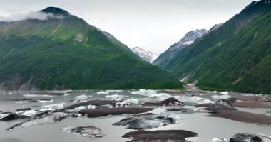 Eriyen buzla dolu nehri olan yemyeşil dağlar. Arka planda karla kaplı taşlar. Alaska vahşi doğa.