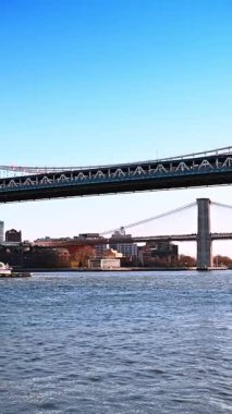 Brooklyn ve Manhattan Köprüleri su manzarası alçak açılı. Köprülerin altından uzun mavna geçiyor. Dikey video.