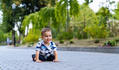 Kaldırım taşlarının üzerinde eğlenceli bir emekleme. Çocuk, yumuşak yeşilliklerle çevrili kaldırım yolunda oynarken diz çöker ve parlak bir şekilde gülümser..