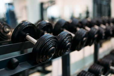 Salon dambılları askıda. Profesyonel bir spor salonunun içindeki metal bir rafa düzgünce yerleştirilmiş ağır dambılların görüntüsünü kapat..