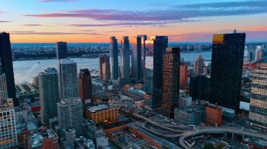 New York gökdelenlerinin tepeleri batan güneşin ışığını yansıtıyor. Gün batımında doğu nehrinin su manzarasına yaklaşıyoruz. Hava görünümü.