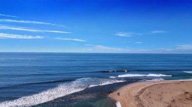 Güneşli bir günde Pasifik Okyanusu 'nun sakin mavi manzarası. Bazı sörfçüler suda. İnsanlar Malibu, California, ABD 'nin kumlu sahillerinden geçiyor. Hava görünümü.