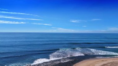 Beyaz köpüklü dalgalar kıyıya vuruyor. Sörfçüler güneşli bir günde Pasifik Okyanusu 'nda pratik yapıyorlar. Malibu, California, ABD. Hava görünümü.