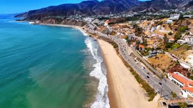 Canlı otoyol boyunca Pasifik Okyanusu 'nun kumlu kıyısında görüntüler. Yamaçlarda birden fazla evi olan Rocky Hills. Malibu, California, ABD.