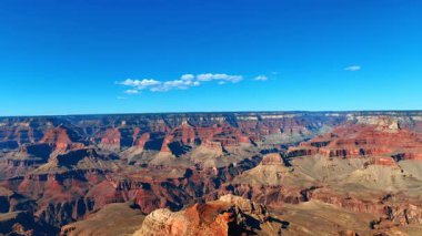 Parlak Mavi Gök Altında Büyük Kanyon Katmanları. Büyük Kanyonlar kızıl kayalıklar ve derin vadiler berrak bir gökyüzünün altında canlı renklerle açılır. Güneş ışığı dramatik jeolojik oluşumları vurguluyor.