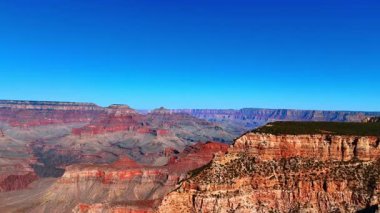 Açık Güneş Işığında Büyük Kanyon Panoraması. Parlak güneş ışığı Büyük Kanyon 'un uçsuz bucaksız derinliğini ve renkli uçurumlarını gözler önüne seriyor. Kırmızının ve altının gölgeleri engebeli arazide uzanıyor..