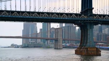 New York, ABD 'deki Manhattan ve Brooklyn Köprüleri. Doğu Nehri 'nin alçak açılı manzarası. Kasvetli, kasvetli arka planda şehir silüeti.