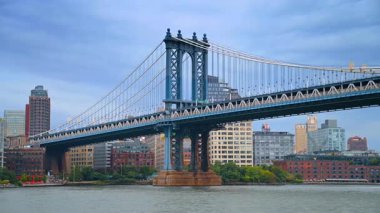 Kasvetli gri bulutlu gökyüzüne karşı çarpıcı Manhattan Köprüsü. Nehir manzarasının alçak açısı. Arkaplanda New York 'un silüeti.