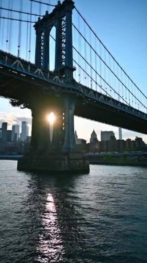 Manhattan Köprüsü 'nün altındaki teknede. Gökdelenler arasında güneş batarken New York 'un silüeti. Dikey video.