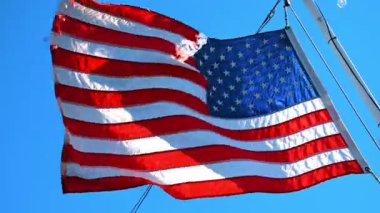 Dışarıda sallanan Amerikan bayrağı rüzgarda dalgalanıyor. Düşük açı. Kapatın. Arkaplanda mavi açık gökyüzü.
