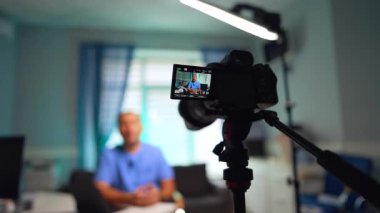 Modern bir kameranın önünde mavi üniformalı bir adam. Tıbbi video blogu oluşturma. Seçici odak.