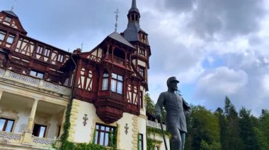 Romanya 'nın Prahova İlçesi' ndeki çarpıcı Peles Şatosu 'nun perdesini yeşillik kaplıyor. Kral Carol 'a alçak açılı bir bakış açısı. Binanın önündeki anıt..