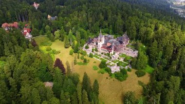 Kafkas dağlarını kaplayan yemyeşil çam ağaçları. Ünlü Peles Şatosu, Prahova Bölgesi, Romanya ormanların arasındaki çayırda duruyor. Hava görünümü.
