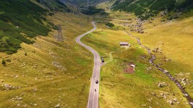Yeşil vadideki dalgalı yolda bir araba ve bisikleti takip ediyorum. Büyüleyici Transfagarash otoyolu ve tepesinde gri bulutlarla kaplı Karpat Dağları 'nın manzarası gözler önüne seriliyor..