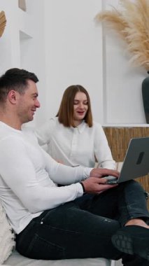 Dizinde dizüstü bilgisayar tutan mutlu ve rahat bir adam ve onu bir bayana gösteriyor. Çift dizüstü bilgisayara bakar ve gülümser. Dikey video