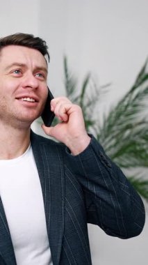 Dirençli, beyaz bir adam telefonda konuşuyor. Ceketli bir adam telefon görüşmeleri sırasında odada durmuş neşeyle gülüyor. Dikey video