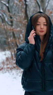 Kışın açık havada yürüyen uzun saçlı esmer. Siyah ceketli bir kız telefonda kahve içip sohbet ediyor. Dikey video