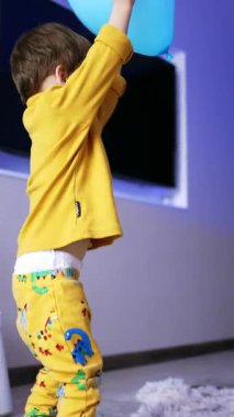 Küçük oğlan yerden büyük mavi bir balon alıyor. Çocuk balonu fırlatmak istiyor ama balon ellerinden kayıp uçuyor. Düşük açı. Dikey video