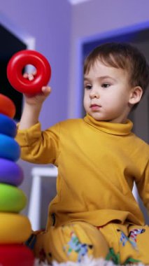 Ciddi bir beyaz çocuk piramidi birleştiriyor. Çocuk oyunu bitirince seviniyor. Düşük açı. Dikey video