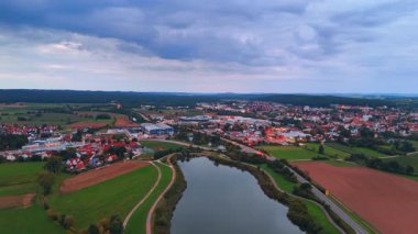 Şehir nehri tarlalarda kıvrılır. Nehir ve şehir, etrafındaki tarlalarla yumuşak bulutların altında uzanıyor.