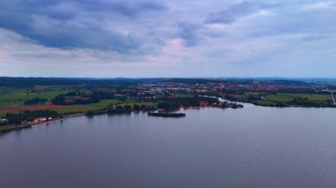 Mavi saatte kasaba ve göl. Kasaba ışıkları dramatik mavi saat bulutlarının altında göl kenarında parlıyor.