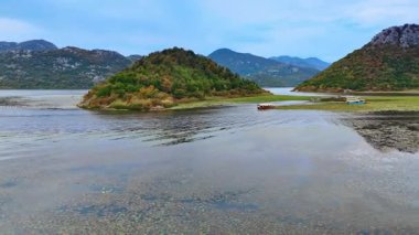 Su zambaklarıyla kaplı dağlardaki gölün üzerinden hızla uçuyordu. Ahırlı kayıklar yemyeşil ağaçlarla kaplı küçük kayalık adanın yanında suyun üzerinde duruyor..