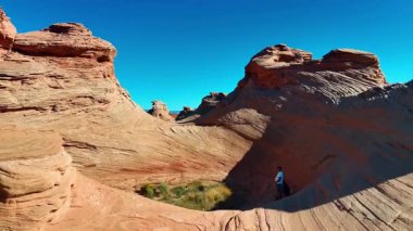 Man stands in the alcove created by the sandstone cliffs of spectacular shape. Drone footage over the weird rock formations in Arizona, near Page, USA.
