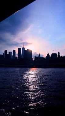 Travel by the dark riverscape at dusk time. Silhouette of modern city skyline at backdrop. Vertical video.