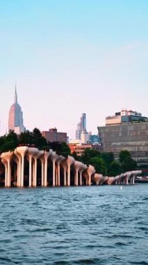 Beautiful green park on the mushroom-like columns at pier 55, New York, USA. Boat travel along the pier at sunset. Vertical video.
