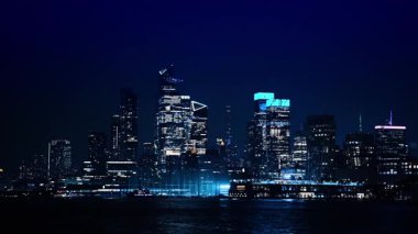 Iconic view of luminous New York skyline at night. Travelling by the dark riverscape of the East River by boat.
