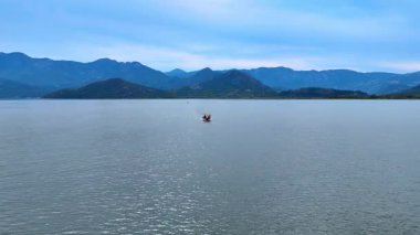 Ulcinj, Montenegro, 14 August 2025: Small boat on lake horizon. A small boat heads across the lake horizon with tall mountains rising behind.
