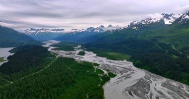 Braided river valley in Alaska mountains. Multiple silver channels of a braided river wind through forested valley toward peaks.