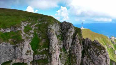 Dangerous cliff rocks of the stunning Bucegi Mountains, Romania. People stand on the top of the mount. The Caraiman Peak with Cross memorial at backdrop.