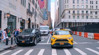 New York, USA, 8 August 2025: Street with cars riding by among the high-rises. An American flag is hanging on the building faade. New York, USA at daytime.